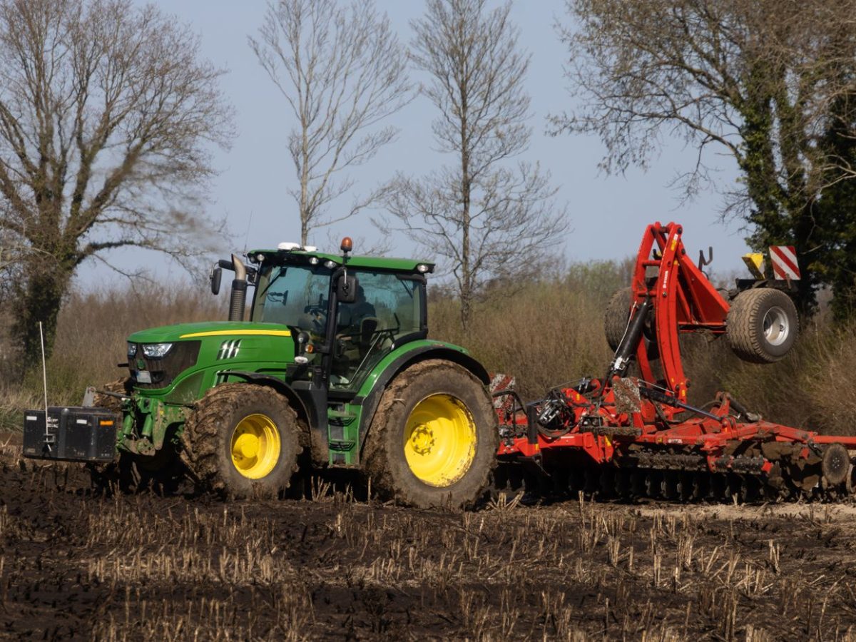 Tractor working a field with a mounted agricultural implement attached to the rear linkage